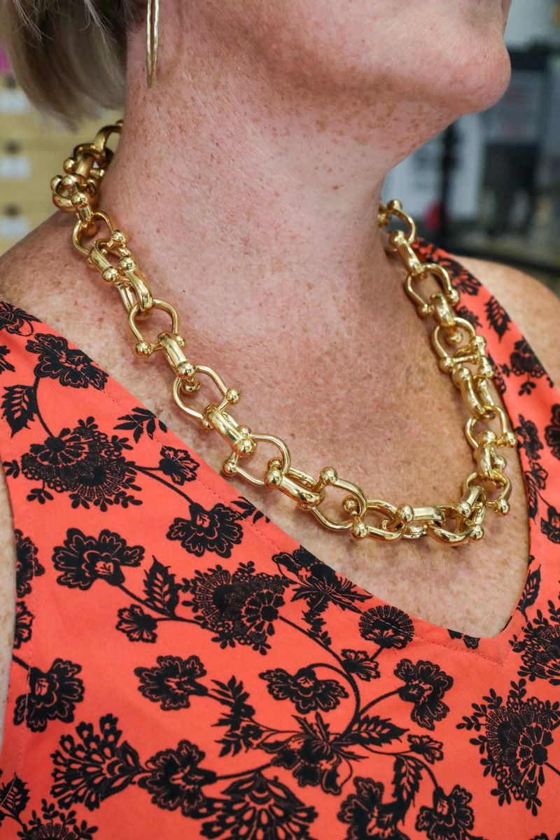 A person wearing a gold chain necklace and an orange top with black floral patterns, ideal attire for exploring Split indoor attractions or discovering rainy day activities in Split.